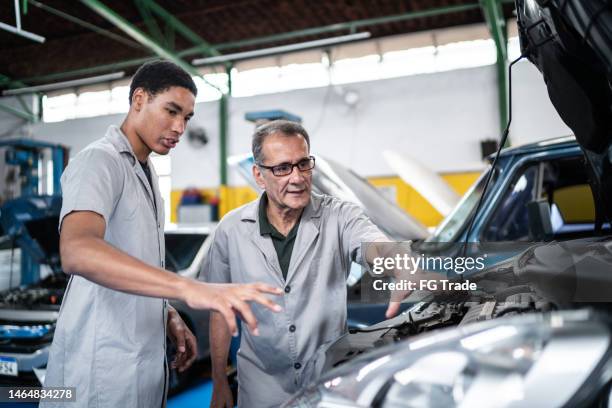 auto mechanic man showing the car engine to his assistant on the repair shop - werk in uitvoering stockfoto's en -beelden