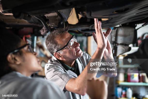 auto mechanic man teaching his assistant on the repair shop - werk in uitvoering stockfoto's en -beelden