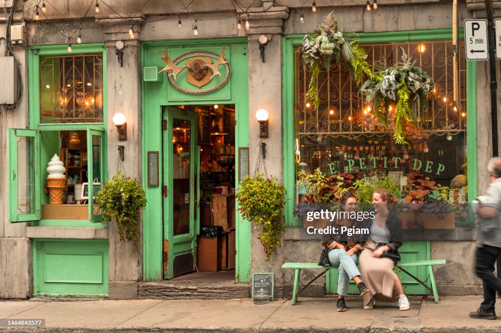Duas mulheres riem em um banco em frente a um restaurante de café tradicional na Cidade Velha de Montreal, Quebec Canadá