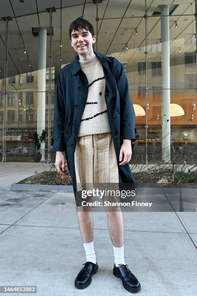 Guest wears a light tan raw-edged kilt, an oatmeal colored sweater, dark navy blue trench, and black oxford shoes at the Kate Spade New York...