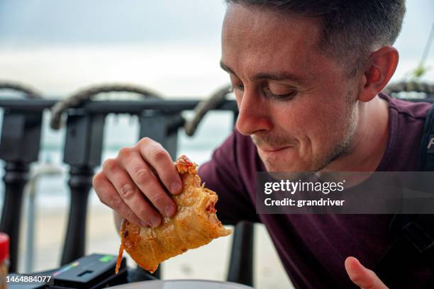 young man in his twenties sitting at a beach-side open air restaurant eating a delicious shrimp taco in tijuana mexico - eating cajun food stock pictures, royalty-free photos & images