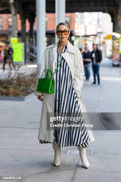 Mary Lawless Lee wears green bag, black white striped button up dress, creme white trench coat, boots, sunglasses outside Kate Spade during New York...