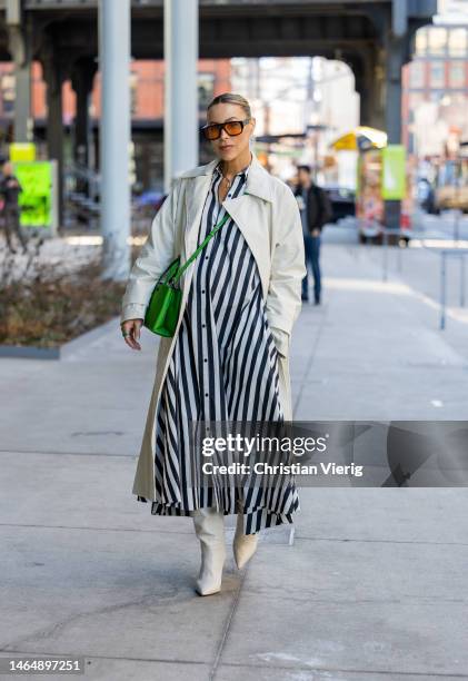 Mary Lawless Lee wears green bag, black white striped button up dress, creme white trench coat, boots, sunglasses outside Kate Spade during New York...