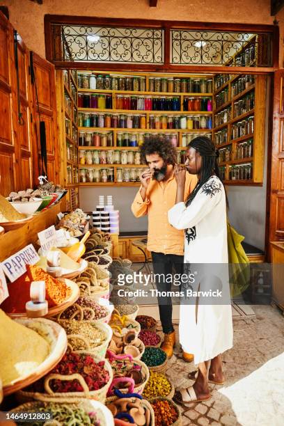 wide shot couple smelling spices while shopping in souks in marrakech - marrakech spice stock pictures, royalty-free photos & images