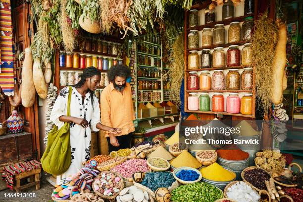 wide shot of couple shopping in spice shop in the souks of marrakech - marrakech fotografías e imágenes de stock