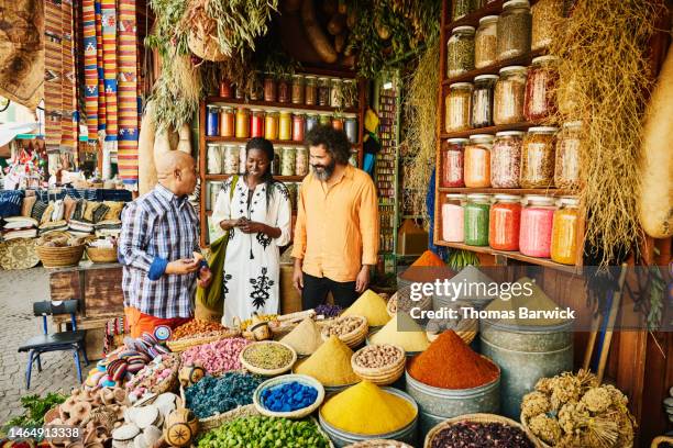 wide shot couple talking to spice shop owner in the souks of marrakech - bazaar stockfoto's en -beelden