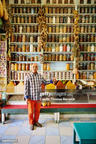 wide shot of spice shop owner standing in front of wall of spices - marrakech spice stockfoto's en -beelden