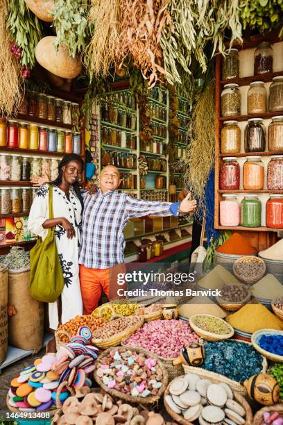 wide shot of smiling woman and spice shop owner in front of spice shop - zoco fotografías e imágenes de stock