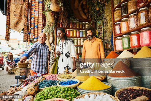 Wide shot couple talking to spice shop owner in the souks of Marrakech