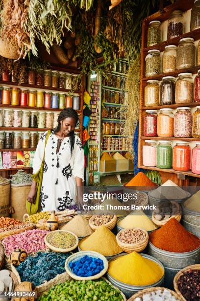 wide shot of woman shopping in spice shop in the souks of marrakech - african shop fotografías e imágenes de stock