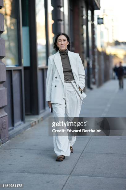 Eva Chen wears gold earrings, a brown ruffled high neck t-shirt, a white ribbed velvet blazer jacket, matching white ribbed velvet large pants, dark...