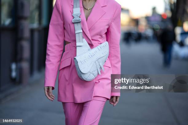 Katya Tolstova wears a gold large chain necklace, a pink cut-out waist long blazer jacket, matching pale pink wide legs suit pants, a pale gray with...