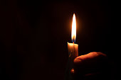 candle flame illuminates a female hand in a dark room