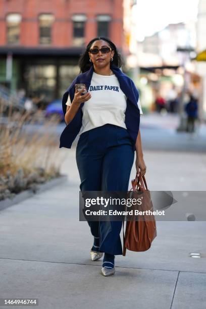 Guest wears dark brown sunglasses, a white with navy blue embroidered Daily Paper slogan pattern t-shirt, a navy blue wool pullover, navy blue large...