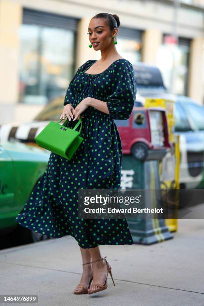 Guest wears green pendant earrings, a black with green polka dots print pattern squared neck / puffy long sleeves / midi dress, a green shiny leather...