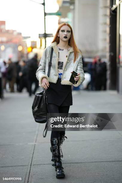 Guest wears a silver nose piercing, a beige with black print pattern t-shirt, a silver shiny leather with beige sheep borders jacket, a black short...