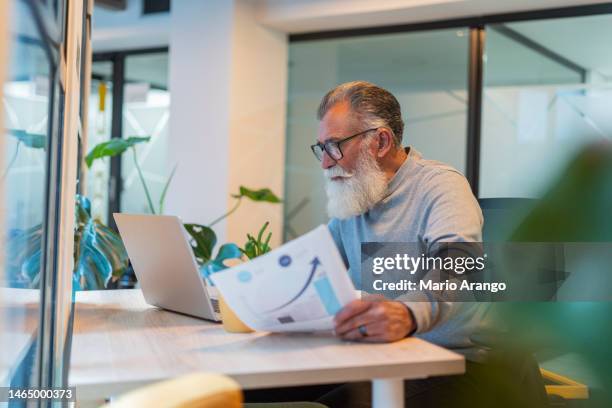 latino man is inside the office where he works with his laptop in his hands with which he does his pending work while standing at the door of his office - pending stock pictures, royalty-free photos & images