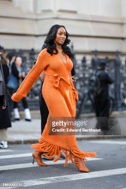 Guest wears an orange braided wool V-neck long sleeves / belted / fringed long dress, camel shiny leather pointed / heels ankle boots , outside...