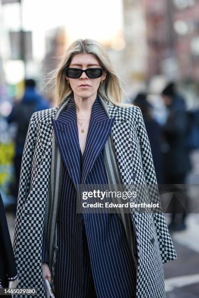 Guest wears black sunglasses, gold earrings, gold chain pendant necklaces, a navy blue with white striped print pattern oversized blazer jacket, navy...