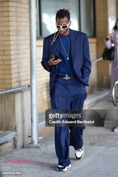 Guest wears white sunglasses, a navy blue t-shirt, a navy blue blazer jacket, matching navy blue suit pants, a black shiny leather with silver large...