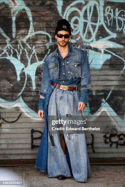 Guest wears a black with embroidered white inscriptions wool beanie, black sunglasses, a blue pearls necklace, a navy blue denim shirt, a blue faded...