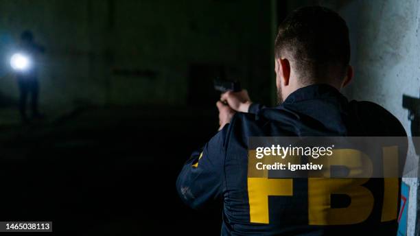 armed fbi agent from the back aiming in a criminal in a dark room - fbi gun stock pictures, royalty-free photos & images