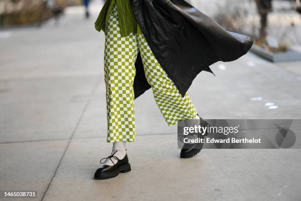 Guest wears a green khaki pleated silk shirt, a black shiny leather long coat, a green shiny leather shoulder bag, green and white checkered print...