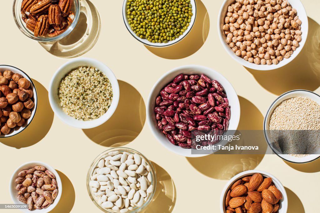 Various kinds of vegan protein sources on beige background. Set of food supplements. Gluten free cereals as ground hemp seeds, quinoa. Nuts and legumes (green mung beans, chick-pea, red lentil, kidney bean, almonds, hazelnuts). Flat lay, top view