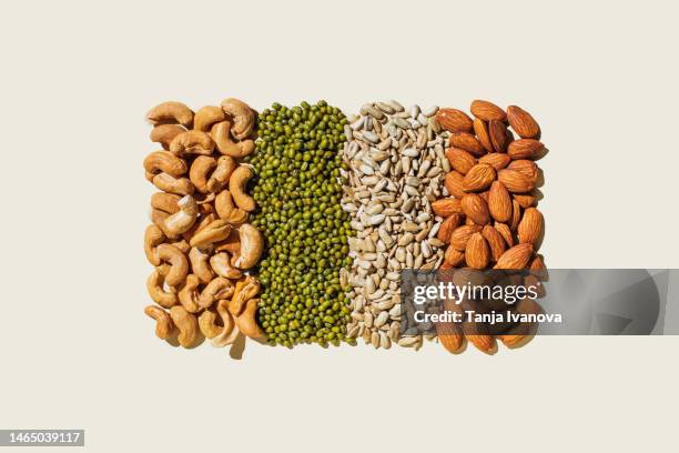 various kinds of vegan protein sources on beige background. nuts and legumes (green mung beans, cashew nuts, almonds, sunflower seeds). flat lay, top view - peulvruchtenfamilie stockfoto's en -beelden