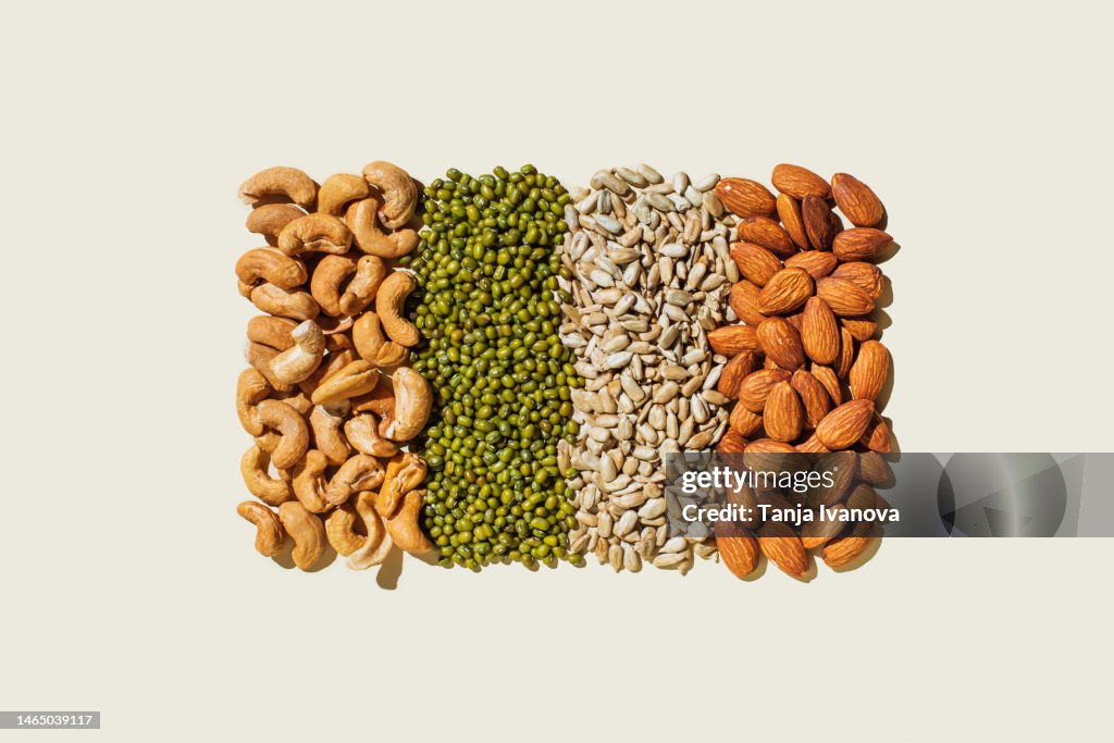 Various kinds of vegan protein sources on beige background. Nuts and legumes (green mung beans, cashew nuts, almonds, sunflower seeds). Flat lay, top view