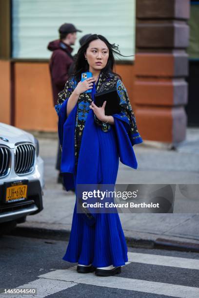 Guest wears a black with blue and yellow print pattern kimono shirt, a royal blue pleated long skirt, a black shiny leather clutch, a white shiny...