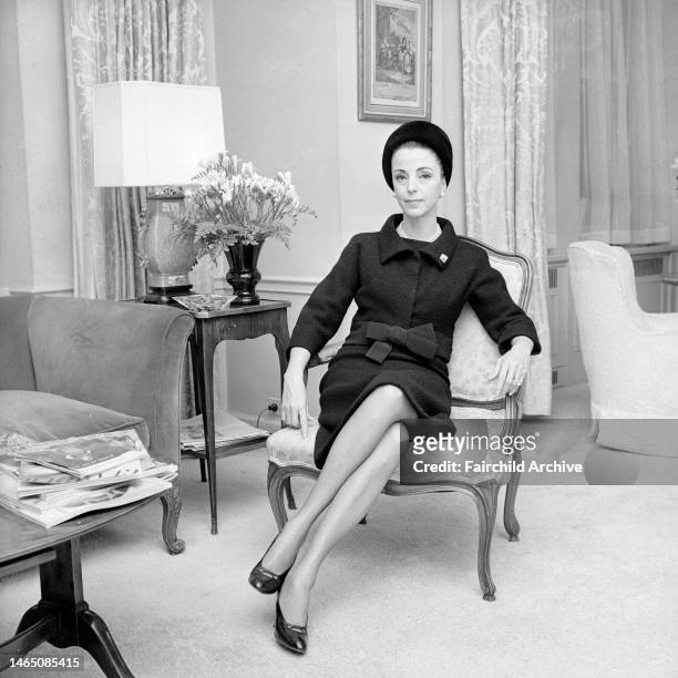Outtake; Gloria Guinness seated in her suite in the Waldorf Towers wearing a black wool Givenchy jacket bordered in black faille over a sleeveless...
