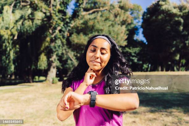 front view portrait of a brunette latin american sport woman, measuring taking her pulse with a smart watch. - tomando el pulso fotografías e imágenes de stock