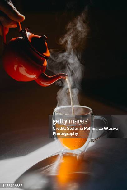 studio shot of teapot pouring hot tea in transparent mug - tea pot stock pictures, royalty-free photos & images