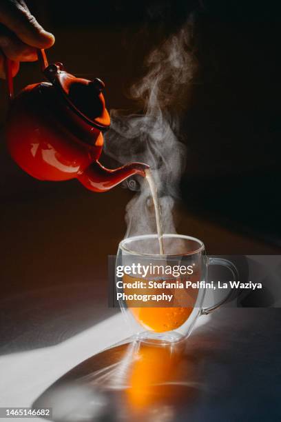 studio shot of teapot pouring hot tea in transparent mug - chamomile tea 個照片及圖片檔