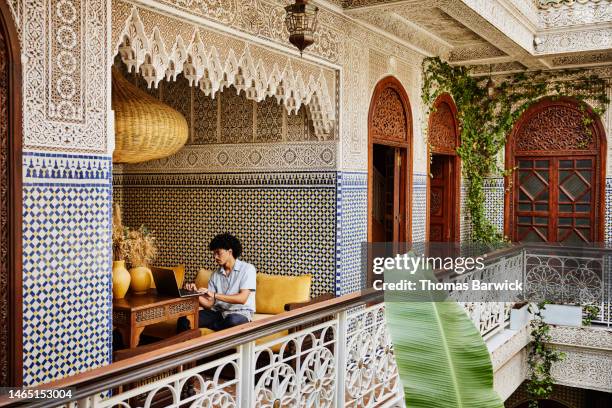 wide shot man working on laptop in riad during vacation in marrakech - premium access image only stock-fotos und bilder