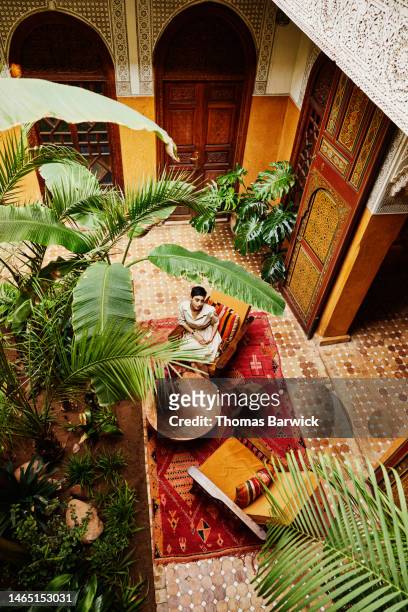 extreme wide shot woman relaxing in riad during vacation in marrakech - majestic hotel stock pictures, royalty-free photos & images