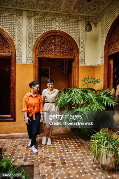 wide shot smiling female couple walking through riad while on vacation - pantalón decorado fotografías e imágenes de stock