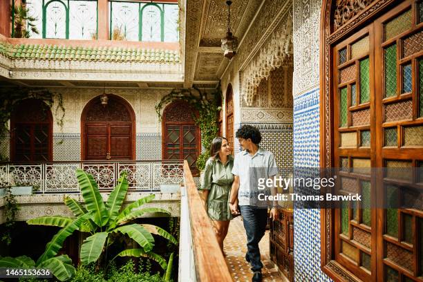wide shot of smiling couple holding hands and walking through riad - moroccan woman stock pictures, royalty-free photos & images