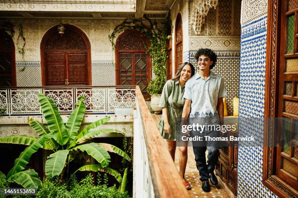wide shot of smiling couple holding hands and walking through riad - arab villa stock-fotos und bilder
