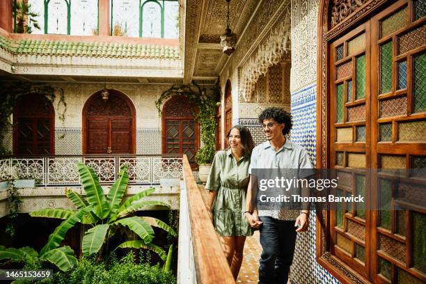 wide shot of smiling couple holding hands and walking through riad - marokko stock-fotos und bilder