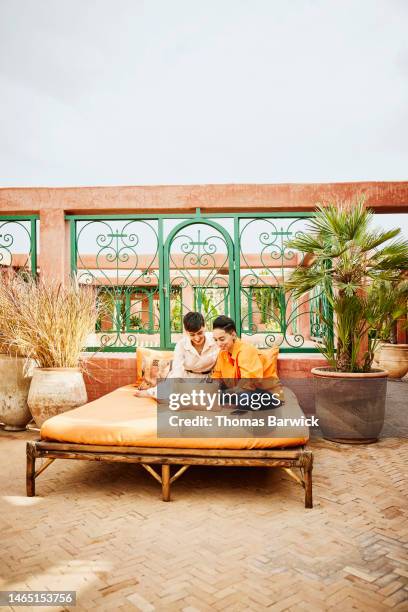 wide shot female couple working on laptop on rooftop terrace of riad - arab villa stock pictures, royalty-free photos & images