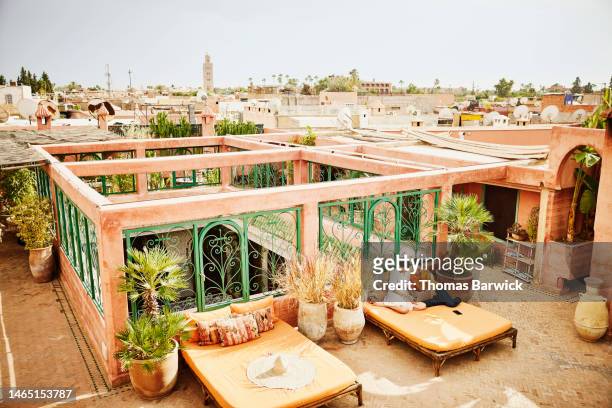 wide shot female couple working on laptop on rooftop terrace of riad - marrakesh stockfoto's en -beelden