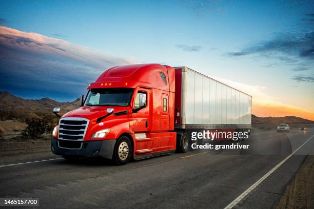 brightly red colored semi-truck speeding on a two-lane highway with cars in background under a stunning sunset in the american southwest - semi truck stockfoto's en -beelden