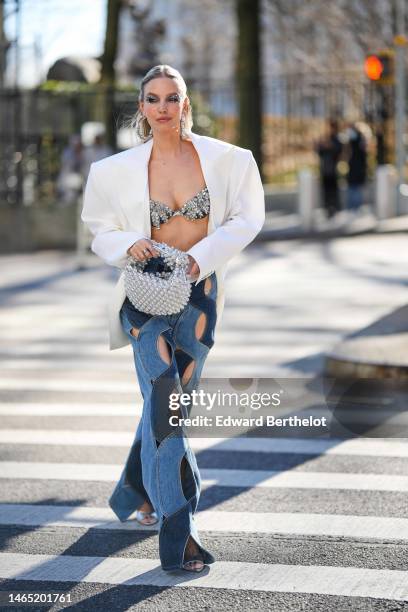 Leonie Hanne wears a long crystals pendant earrings, a black with embroidered crystals bra underwear from Area, a white shoulder-pads oversized...