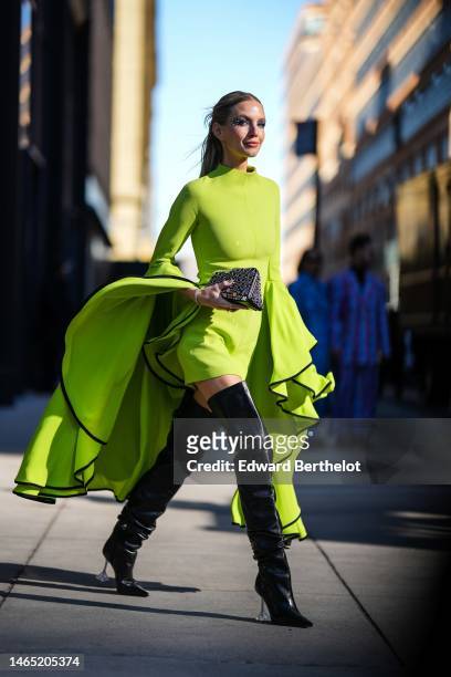 Leonie Hanne wears a green high neck / long oversized ruffled sleeves / short dress, a black shiny leather mirror nailed / studded clutch, black...