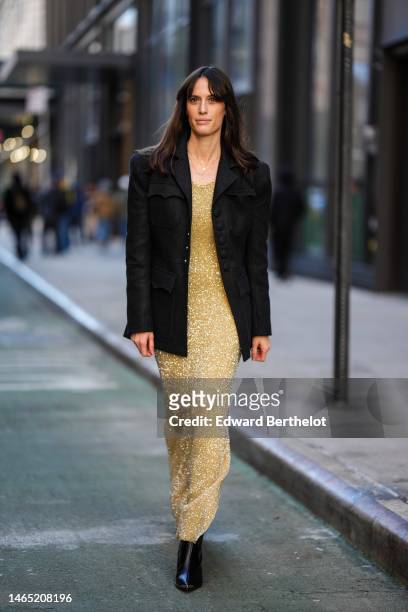 Astrid Boutrot wears a black buttoned blazer jacket, gold necklaces, a gold glitter long tube dress, black shiny leather varnished pointed heels...