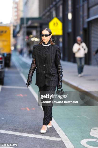 Guest wears black futurist sunglasses, a black striped print pattern blazer jacket, a crystal large necklace, lack shiny leather high gloves, black...