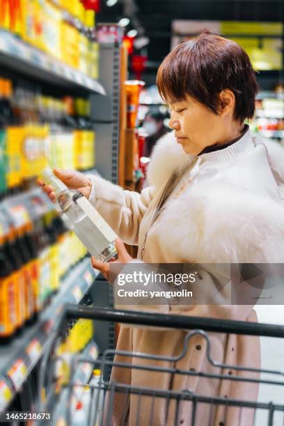 a middle-aged woman checks whether the white vinegar label on the market has no additives - healthy life, healthy diet - food dressing stock pictures, royalty-free photos & images