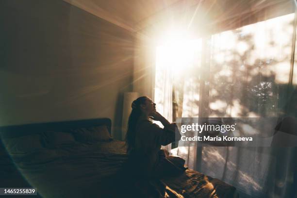 young woman in bathrobe who has just woken up enjoys the rays of the morning sun. - aufwachen stock-fotos und bilder